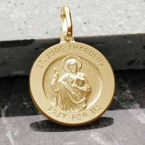 May include: Gold-toned St. Jude Thaddeus medal pendant with a raised image of the saint holding a book and a staff. The medal is inscribed with "St. Jude Thaddeus" and "Pray for Us".