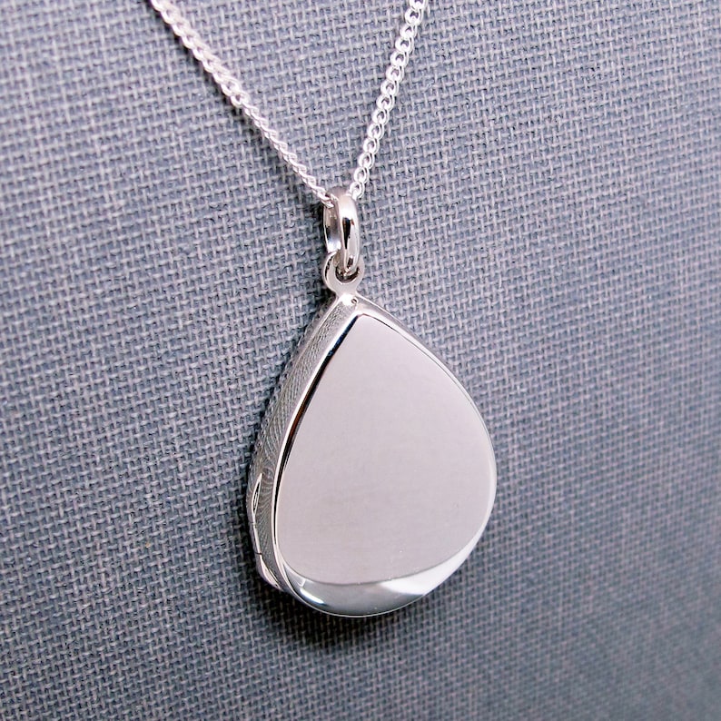 May include: A silver teardrop-shaped locket pendant on a silver chain.