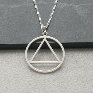 May include: A silver-colored pendant necklace featuring a geometric design. The pendant has a circle with a triangle inside, and a horizontal line at the bottom of the triangle. The necklace chain is also silver.