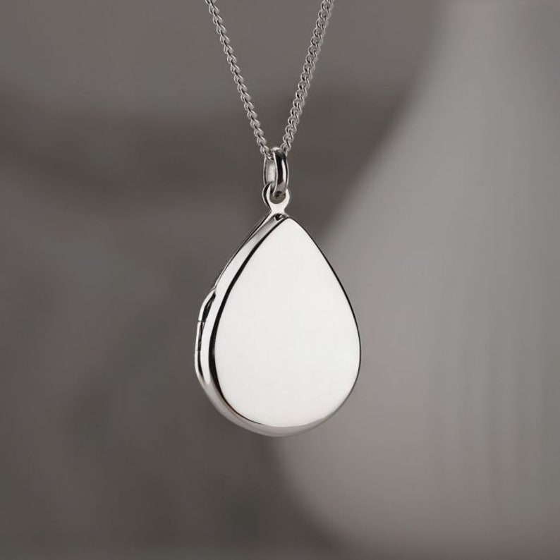 May include: A silver teardrop-shaped locket pendant on a silver chain.