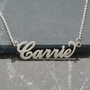 May include: A silver necklace with the name "Carrie" spelled out in a cursive font.