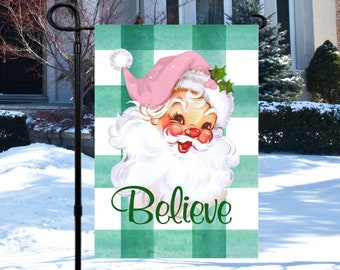 May include: A green and white checkered Christmas garden flag with a vintage illustration of Santa Claus with a pink hat and the word "Believe" in green text.