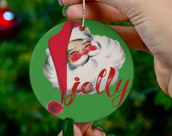 May include: A green and red Christmas ornament with a vintage illustration of Santa Claus's face and the word "jolly" in red cursive lettering.