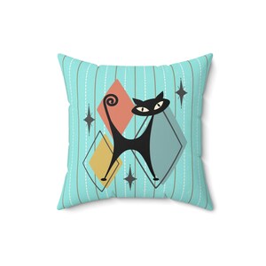 May include: A turquoise blue throw pillow with a black cat design. The cat is stylized with a long tail and large eyes. The background features a geometric pattern of diamonds in shades of blue, yellow, and red.