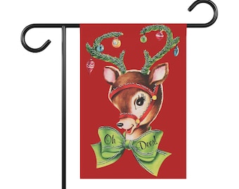 May include: A rectangular garden flag featuring a red background with a central illustration of a brown deer head. The deer has green pine branch antlers decorated with colorful ornaments and a large green bow with the text Oh Deer! printed on it.