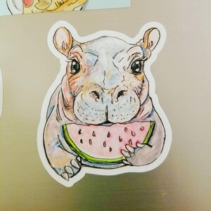 May include: A cartoon illustration of a hippopotamus with a pink watermelon slice in its mouth. The hippo is drawn in a watercolor style with shades of gray, pink, and green.
