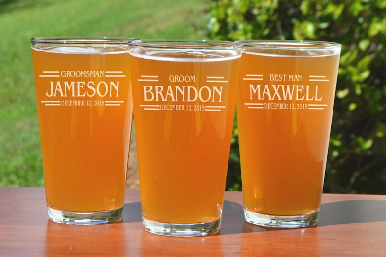 Puede incluir: Tres jarras de cerveza de vidrio transparente con texto personalizado. Las jarras est&aacute;n llenas de una bebida de color &aacute;mbar claro. El texto en las jarras dice "Groom, Best Man y Groomsman" con nombres y la fecha "December 12, 2015".