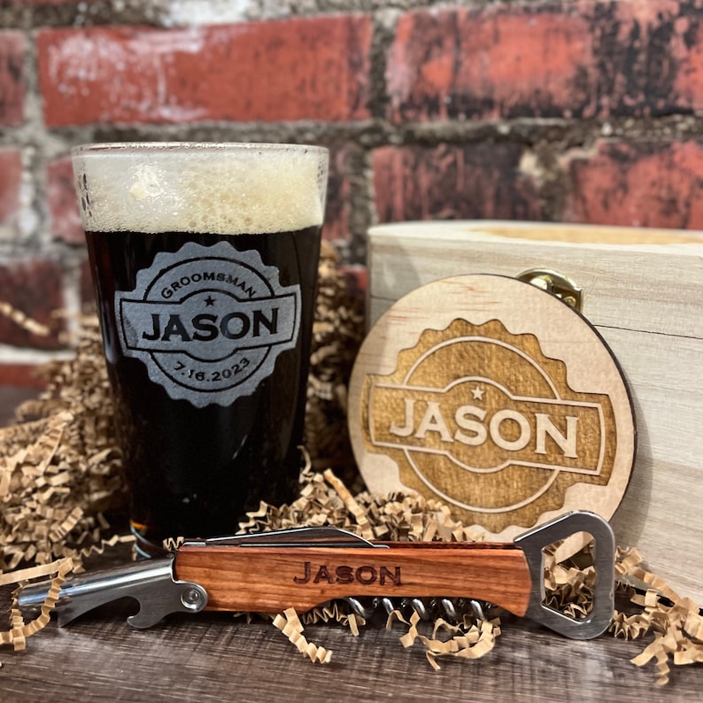 Puede incluir: Un set de regalo personalizado para un padrino de boda con una caja de madera, un vaso de cerveza, un posavasos y un abridor de botellas. El vaso y el posavasos est&aacute;n grabados con el nombre "Jason" y la fecha "7.16.2023". El abridor de botellas tambi&eacute;n est&aacute; grabado con el nombre "Jason".