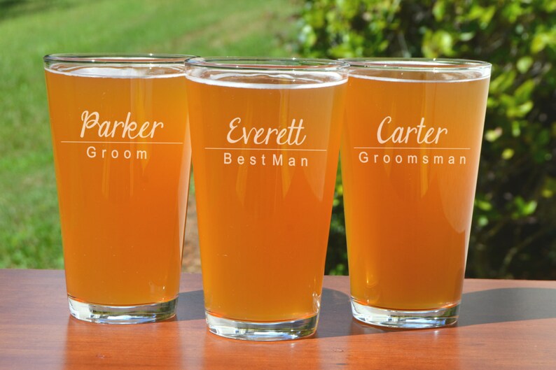 Puede incluir: Tres jarras de cerveza de vidrio transparente con los nombres "Parker Groom", "Everett Best Man" y "Carter Groomsman" grabados en ellas. Las jarras est&aacute;n llenas de una bebida de color &aacute;mbar claro.