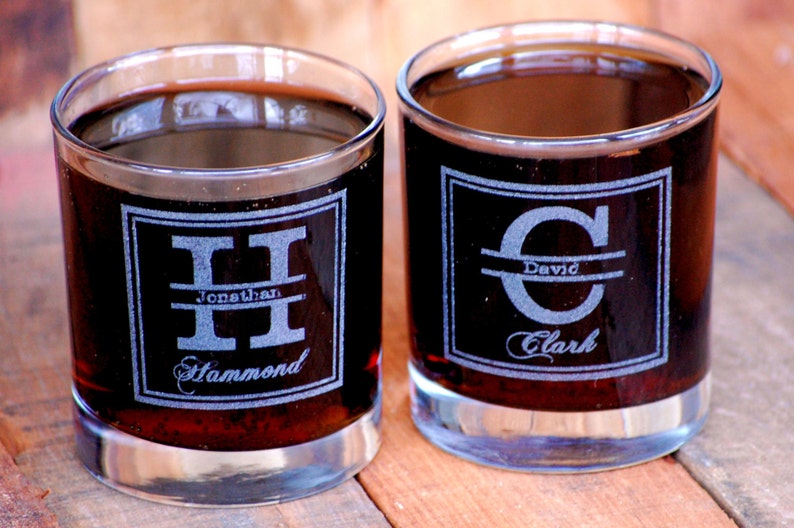 May include: Two clear glass tumblers filled with a dark liquid. Each tumbler features a personalised monogram with a name and initial etched into the glass.