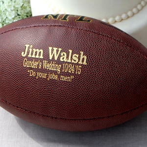 May include: A brown leather football with gold lettering that reads "Jim Walsh, Gunder's Wedding 10.24.15, 'Do your jobs, men!'".