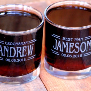 May include: Two clear glass tumblers with engraved text. The tumbler on the left says "Groomsman Andrew 08.06.2016". The tumbler on the right says "Best Man Jameson 08.06.2016".