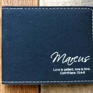 May include: A black leather wallet with white stitching. The wallet has the name "Marcus" and the quote "Love is patient, love is kind. Corinthians 13:4-8" engraved on the front.