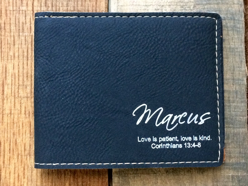 May include: A black leather wallet with white stitching. The wallet has the name "Marcus" and the quote "Love is patient, love is kind. Corinthians 13:4-8" engraved on the front.