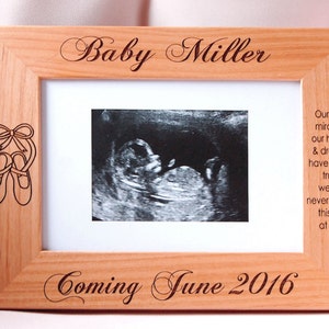 May include: A wooden photo frame with a personalized inscription that reads "Baby Miller Coming June 2016". The frame features a small engraved design of ballet shoes and a black and white ultrasound image.