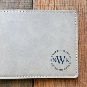 May include: A gray leather wallet with a stitched border and a circle monogrammed with the initials "N.W.K."