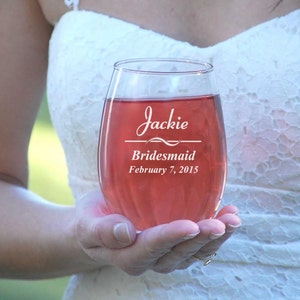 May include: A clear glass wine glass with the text "Jackie Bridesmaid February 7, 2015" etched on the side. The glass is filled with a pink beverage.
