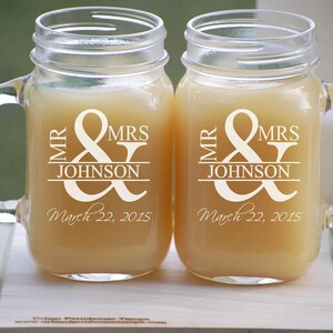 May include: Two clear glass mason jar mugs with handles. The mugs are engraved with the text "Mr. & Mrs. Johnson" and the date "March 22, 2015".