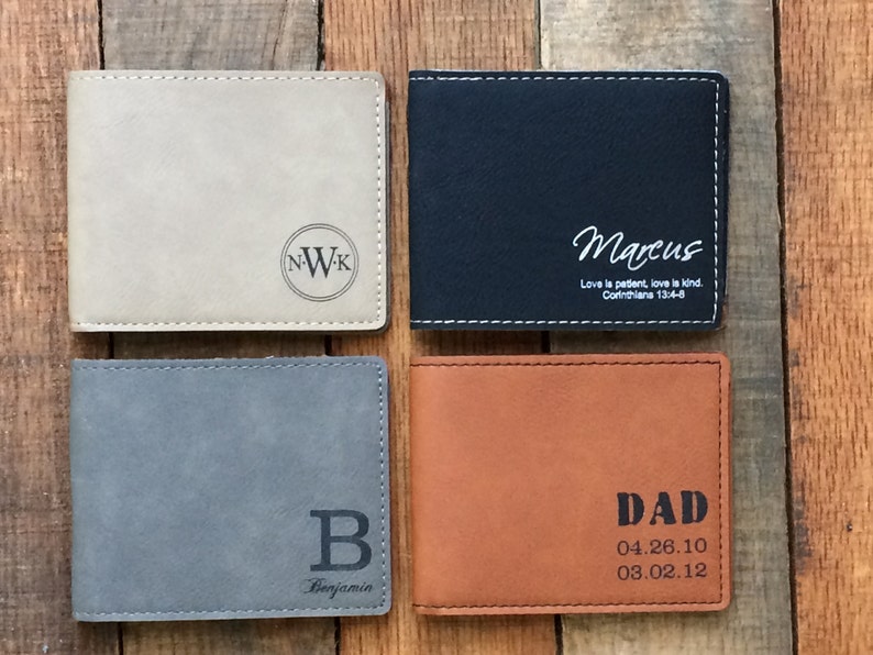 May include: Four different leather wallets with personalized engravings. The wallets are in beige, black, gray, and brown. The engravings include initials, names, dates, and a bible verse.