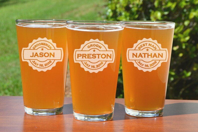 Puede incluir: Tres jarras de cerveza de vidrio transparente con etiquetas personalizadas. Las etiquetas son blancas con texto negro y una estrella. Las jarras est&aacute;n llenas de una bebida de color &aacute;mbar claro. Las etiquetas dicen "Groom, Preston, July 16, 2016", "Best Man, Nathan, July 16, 2016", y "Groomsman, Jason, July 16, 2016".