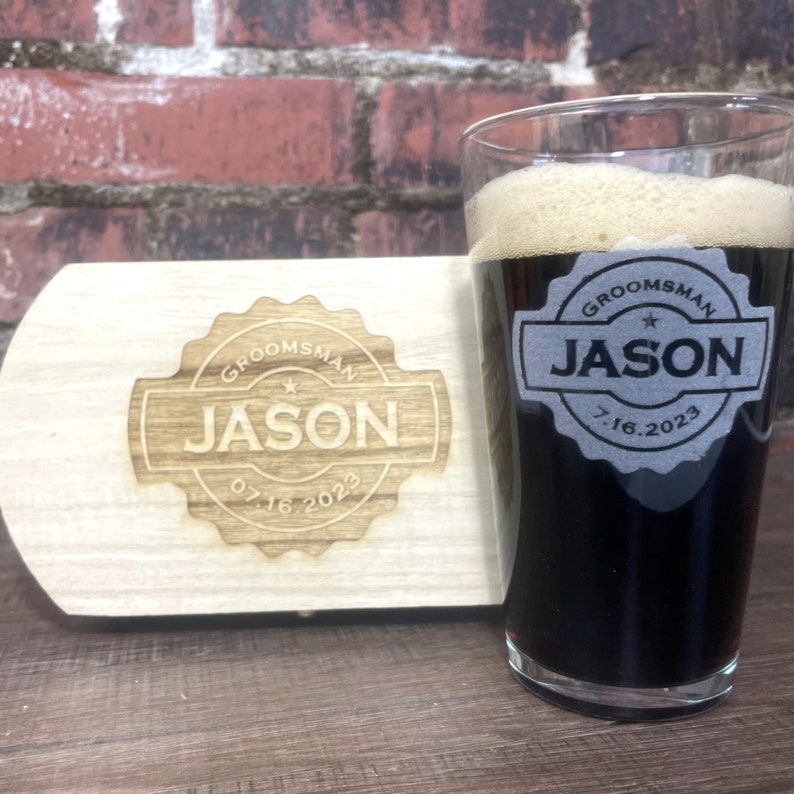 Puede incluir: Una caja de madera con un dise&ntilde;o de padrino de boda grabado con l&aacute;ser. La caja tiene un vaso transparente con un l&iacute;quido negro en su interior. El vaso tiene un dise&ntilde;o de padrino de boda grabado con l&aacute;ser con el nombre Jason y la fecha 07.16.2023.