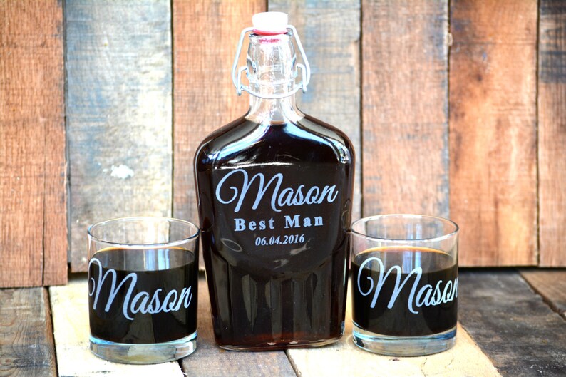 Op de afbeelding: Een gepersonaliseerde glazen likeurfles met een schroefdop en twee bijpassende glazen. De fles en de glazen zijn gegraveerd met de naam "Mason" en de tekst "Best Man 06.04.2016".