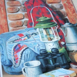 Op de afbeelding: Een vintage-achtige kampeerscène met een rood geruit overhemd, een blauwe rugzak, een groene lantaarn, een verrekijker, een metalen mok, een kaart en een doos lucifers.