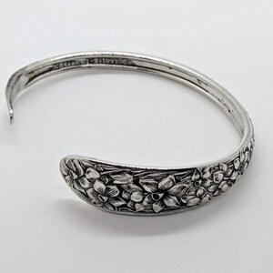 May include: A silver cuff bracelet with a floral design. The bracelet is engraved with flowers and leaves. The text "National Silver Co." is visible on the bracelet. The bracelet is open and has a curved shape.
