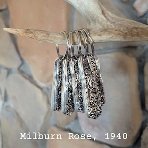 May include: A collection of silver keychains made from vintage silverware, each with an ornate floral pattern. The keychains are hanging from a natural antler. The text "Milburn Rose, 1940" is visible at the bottom of the image.