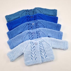 Pode incluir: Cinco cardigans de malha para bebé em tons de azul, do azul claro ao azul escuro, com fechos de botão.
