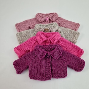 May include: Three knitted cardigans in pink, beige, and purple with button closures. The cardigans have a collar and are made with a fine knit stitch.