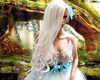 May include: A white and light blue tulle gown with a floral waist detail. The dress features a lace bodice and a flowing skirt. A mannequin head is adorned with a long, white wig and a blue flower.