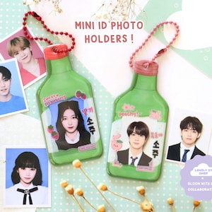Könnte beinhalten: Zwei grüne und rosafarbene, flaschenförmige Fotohalter aus Plastik mit einer Kette. Die Halter haben ein transparentes Plastikfenster zum Einsetzen eines Fotos. Der Text "Sweet Strawberry" und "Peachy!" ist auf den Flaschen aufgedruckt. Der Text "딸기 소주" und "복숭아 소주" ist auf den Flaschen aufgedruckt.