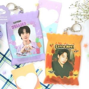 Puede incluir: Dos llaveros de plástico transparente con forma de bolsas de aperitivos. Uno es morado con el texto "CUTIEBO JELLIES" y una foto. El otro es naranja con "Extra Hot!" y una foto. Ambos tienen llaveros.