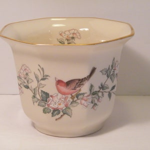 May include: A white ceramic planter with a gold rim and a floral design featuring a pink bird and white flowers.