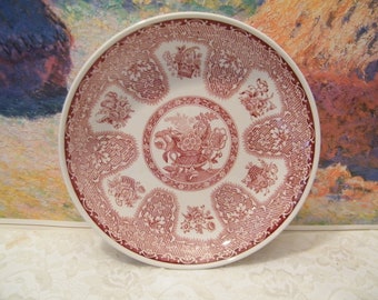 May include: A white ceramic plate with a pink floral design. The plate has a scalloped edge and a raised center with a basket of fruit.