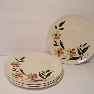 May include: Three white ceramic saucers with a floral design. The design features green leaves, orange and yellow flowers, and brown accents.