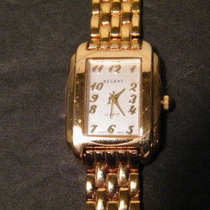 May include: A gold-tone Regent quartz wristwatch with a rectangular face and a gold-tone metal band.