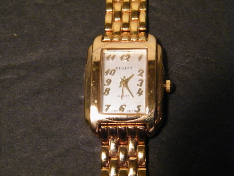 May include: A gold-tone Regent quartz wristwatch with a rectangular face and a gold-tone metal band.