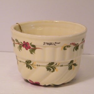 May include: Cream-colored ceramic bowl with a fluted design and hand-painted floral pattern. The bowl features a repeating pattern of red flowers and green leaves. Text on the bowl reads "handpainted in Portugal for California".