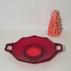 May include: A red glass serving dish with two handles. The dish has a scalloped edge and a raised center.