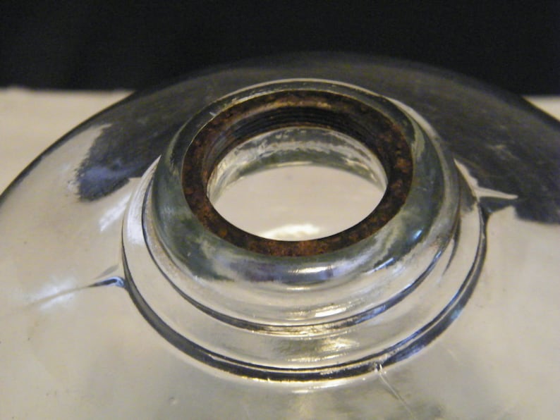 May include: Close-up of a clear glass lampshade with a rusty metal ring around the top opening.