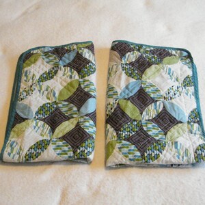 May include: Two quilted pillow covers with a geometric pattern of circles in shades of green, blue, and brown on a white background. The covers have a teal border.