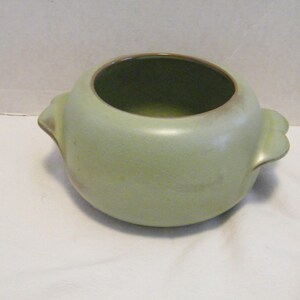May include: A green ceramic planter with two handles. The planter has a brown rim and a slightly textured surface.