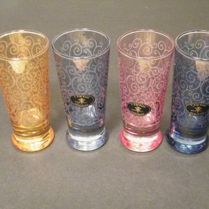 May include: Four glass shot glasses with a swirl design. The glasses are in four different colors: orange, blue, pink, and purple.