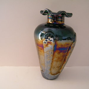 May include: A dark green iridescent glass vase with a ruffled top and a bulbous body. The vase has a unique, textured surface with a metallic sheen.