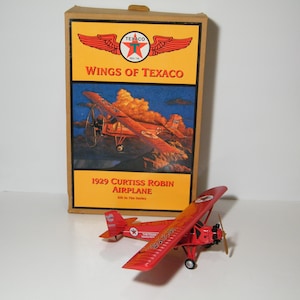 May include: A red 1929 Curtiss Robin airplane model with a Texaco logo on the side. The model is in a box with a picture of the airplane and the words "Wings of Texaco" on the front.