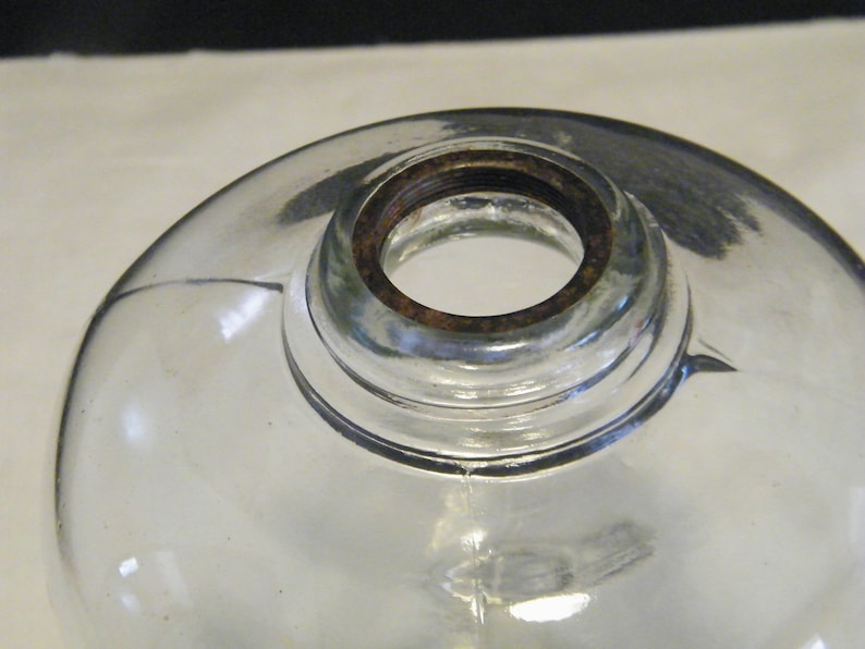 May include: A clear glass globe with a rusty metal rim around the opening. The globe is designed for a lamp or light fixture.