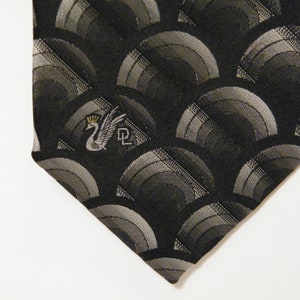 May include: Black silk tie with a silver and grey geometric pattern and a silver swan logo with a crown.