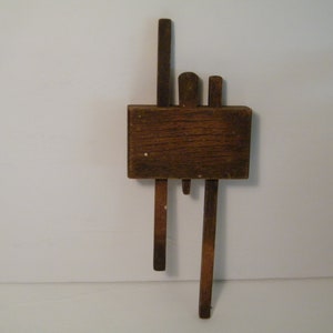 May include: A wooden doorstop with three wooden pieces attached to a rectangular wooden base. The doorstop is brown and has a rustic appearance.